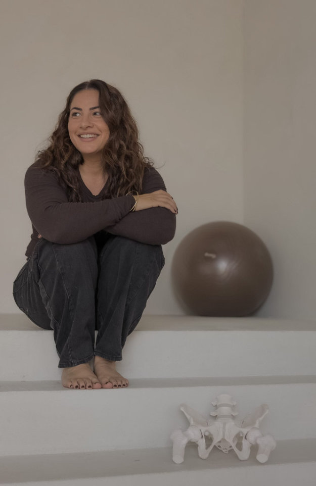 Photo of Susanna Alvarado crouching on white steps beside a birth ball and an anatomical pelvis model